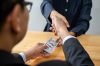 Businesspeople shaking hands to receive banknote money and terms of contract from bribe employer in signing contract while making corruption